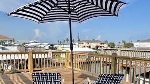 Une terrasse en bois avec deux chaises longues et un grand parasol à rayures.