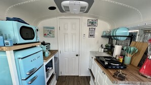 Une petite cuisine équipée avec un four à micro-ondes, un grille-pain et un petit four. On y trouve un plan de travail en bois, un évier et divers ustensiles de cuisine.