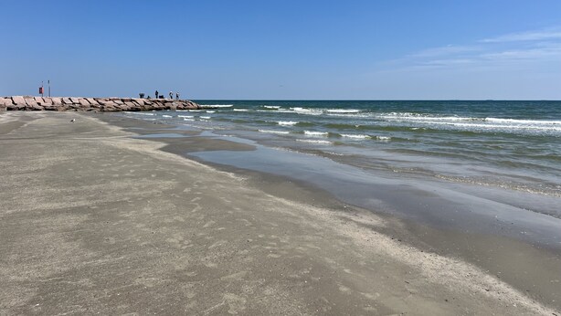 Une plage avec une digue rocheuse et des vagues calmes.