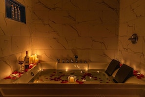 A bathtub with rose petals, candles, and bottles, suggesting a romantic setting.