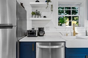 A modern kitchen with stainless steel appliances, a coffee maker, and a window with a view of greenery.