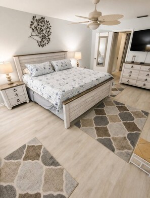 A bedroom with a bed, nightstands, a ceiling fan, a dresser, and a television.