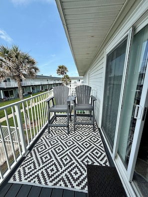A balcony with Adirondack chairs, a patterned rug, and a view of neighboring buildings.