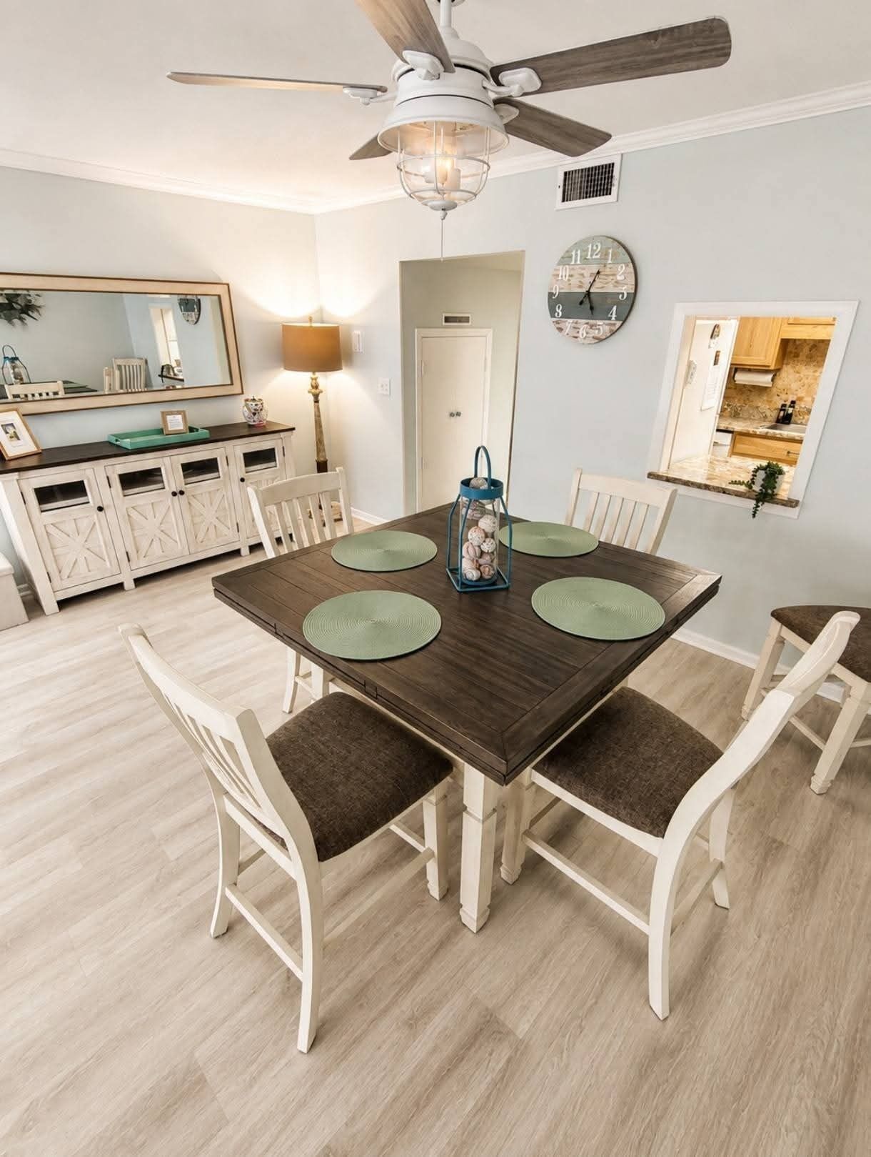 Un comedor con mesa de madera, sillas blancas y ventilador de techo.