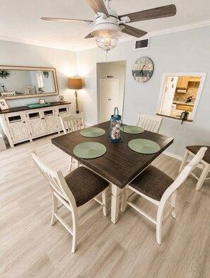 A dining area with a wooden table, white chairs, and a ceiling fan.