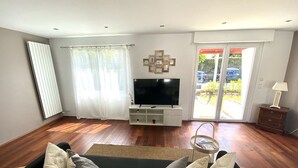 A living room with a flat-screen TV, a sofa, and a coffee table. There is a sliding glass door leading to an outdoor area. - Superbe Maison - Biarritz/plage (Biarritz)