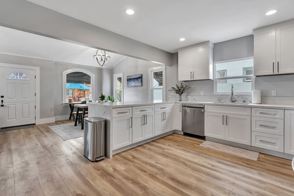 A modern kitchen with white cabinets, a stainless steel dishwasher, and a wooden floor.