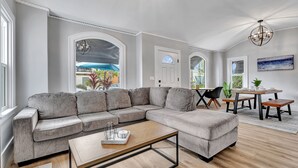 Ein geräumiges Wohnzimmer mit einem großen grauen Ecksofa, einem Holztisch und einem Essbereich mit Tisch und Stühlen.