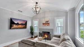 Ein Wohnzimmer mit Kamin, einer Couch, einem Fernseher und Kunstwerken an den Wänden.