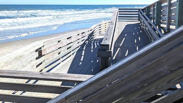 Un paseo marítimo de madera que lleva a una playa, con olas rompiendo en la orilla.