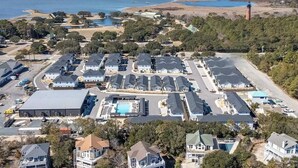 Vista aérea de una zona residencial con varias casas, una piscina y un faro al fondo.