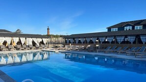 Una piscina con sillas de descanso y un edificio con un faro al fondo.