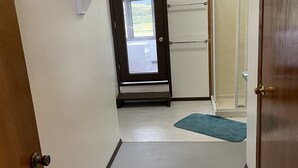 Un corridoio stretto con una porta in legno a sinistra, una porta in vetro che mostra l'esterno e un tappetino blu sul pavimento.