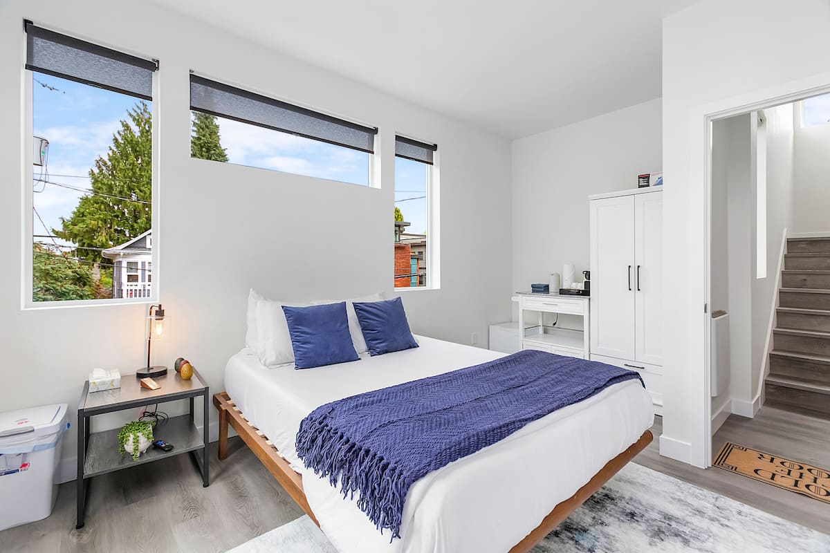 A modern bedroom with a large bed, a nightstand, a desk, and a wardrobe.
