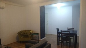 Een woonkamer met een bank, fauteuil en een eettafel met stoelen.