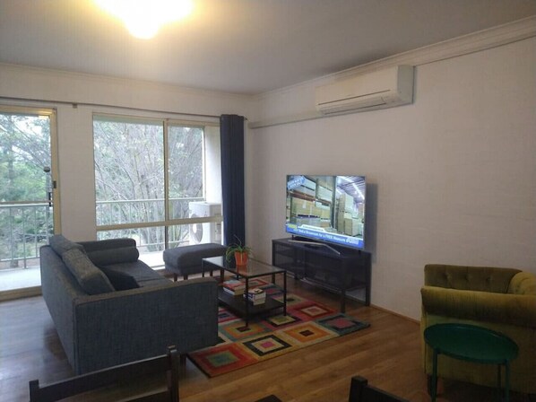 Een woonkamer met een bank, fauteuil, salontafel, televisie en een groot raam.