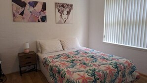 Een slaapkamer met een bloemenbedekte matras, een nachtkastje met een lamp en twee kunstwerken aan de muur.