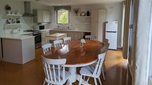 A modern kitchen with white cabinetry, a central island, and a round wooden dining table with white chairs. - Happy & Spacious Home (nr hospital) @Garran (Garran)