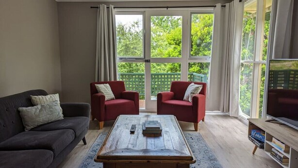 A living room with a dark sofa, two red armchairs, a wooden coffee table, and a TV stand. - Happy & Spacious Home (nr hospital) @Garran (Garran)