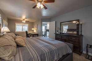 A bedroom with a bed, a dresser, a desk, and a ceiling fan.