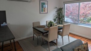 Ruokailutila, jossa on pöytä ja tuolit, ilmastointilaite, kehystetty taulu ja ikkuna, josta avautuu näkymä puihin.