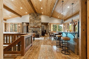 Une cuisine spacieuse avec une cheminée en pierre, des poutres apparentes en bois au plafond et un coin bar avec des tabourets.