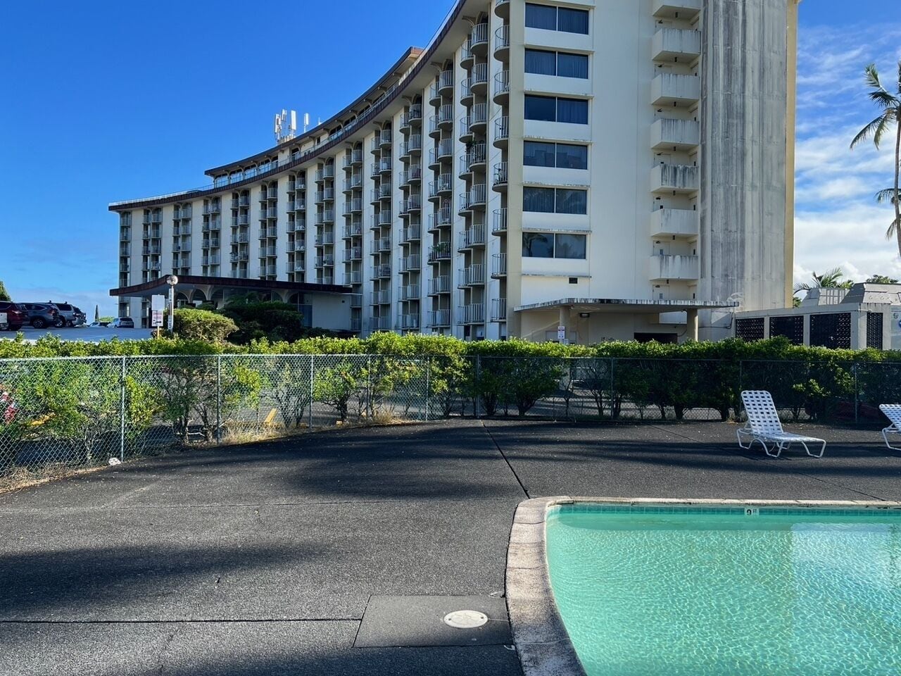 A hotel with a curved facade, a swimming pool, and lounge chairs.