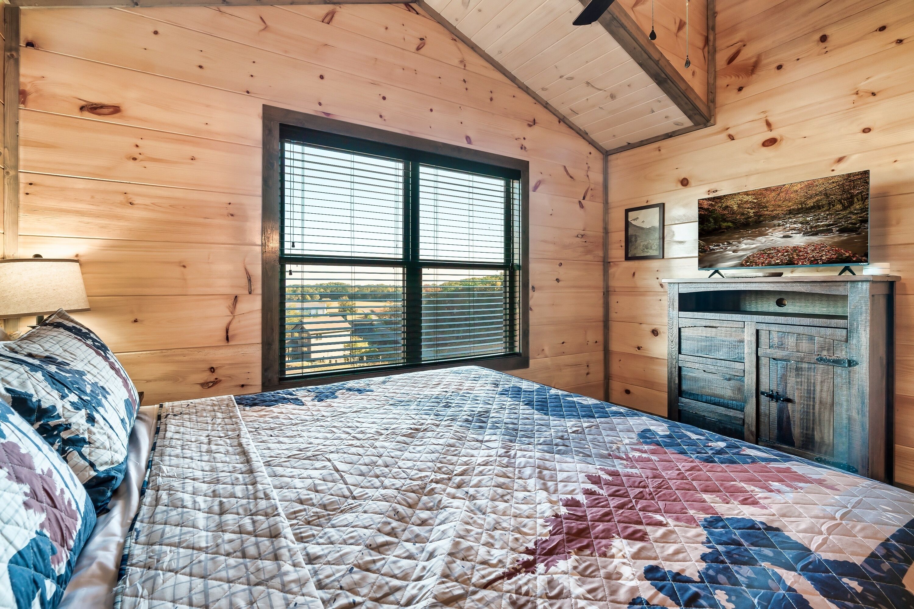 Una camera da letto con un letto grande, una cassettiera in legno, un televisore su un mobile e una finestra con persiane.