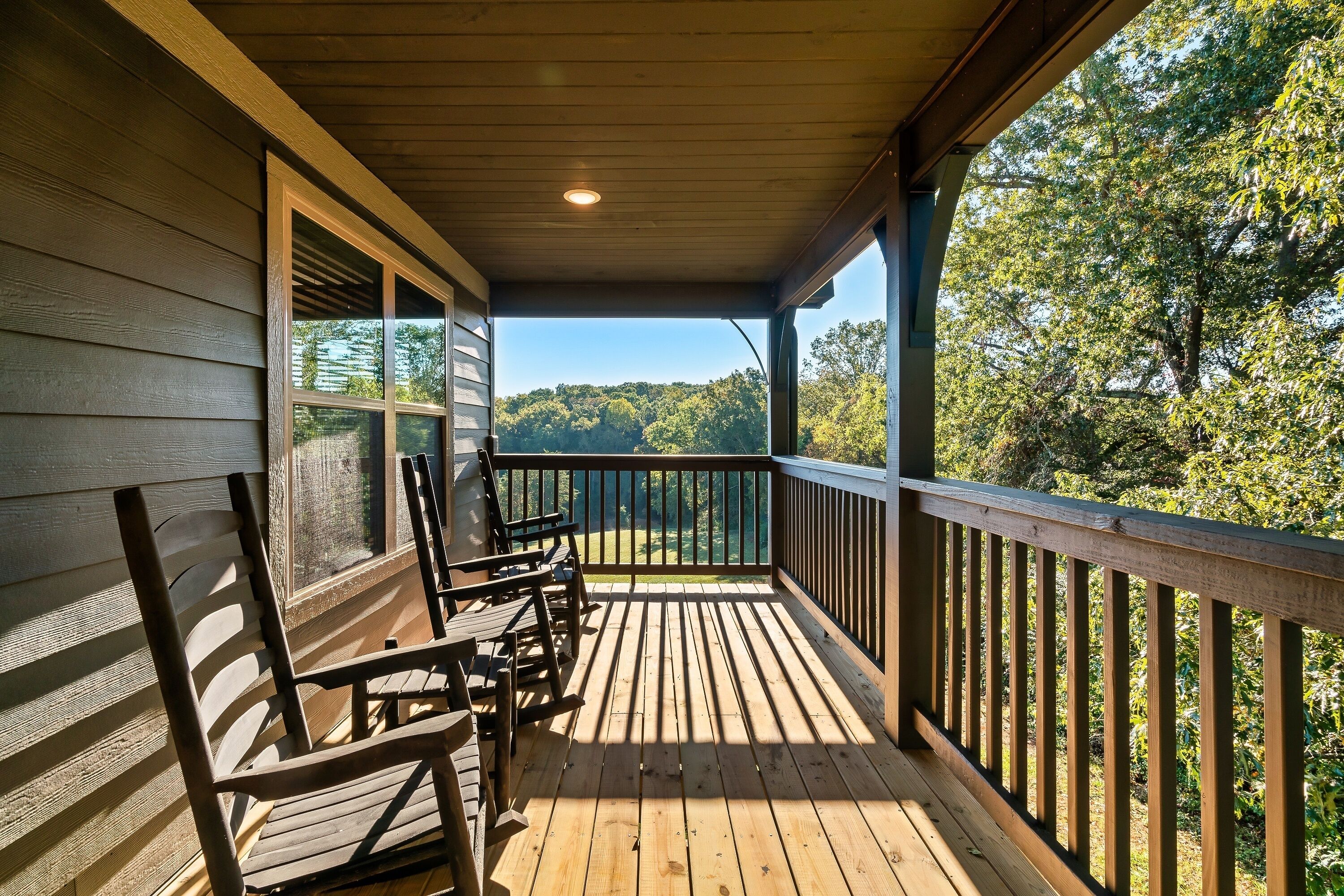A wooden deck with a railing, a bench, and a view of a forested area.
