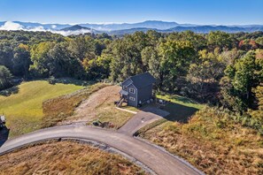 A house with a driveway and a road curving around it, surrounded by trees and mountains in the background.