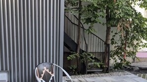 Deux chaises d’extérieur ornées d’un motif géométrique, une clôture en métal et un arbre dans une cour.