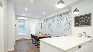 Une cuisine moderne dotée d’un îlot central, d’un coin repas avec une table en bois et d’un mur orné d’un motif de feuilles.