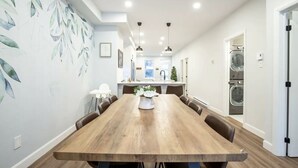 Un vaste espace dédié à la salle à manger, avec une longue table en bois entourée de chaises, et une cuisine en arrière-plan.