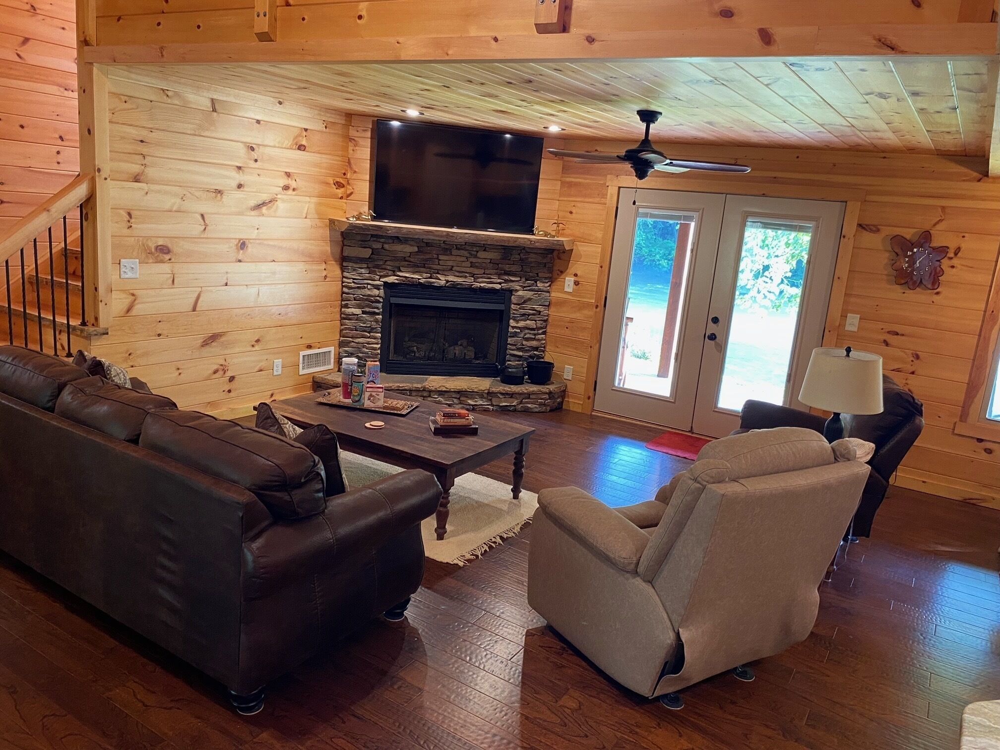 Ein gemütliches Blockhaus-Interieur mit Kamin aus Stein, Ledersofas und einem Flachbildfernseher.