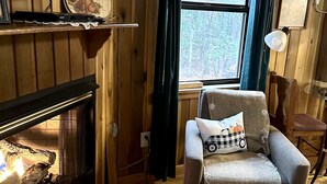 A cozy room with a fireplace, a comfortable armchair, a television, and a window with curtains. - Private cozy cabin in the woods with great view! (Murphy)