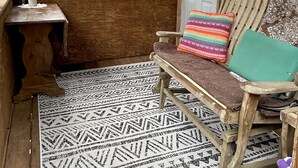 A wooden cabin with a bench and a door, a window overlooking a forest, and a patterned rug on the floor. - Private cozy cabin in the woods with great view! (Murphy)