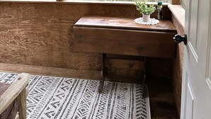 A wooden bench with a small table and a potted plant, a door, and a view of a forest through a window. - Private cozy cabin in the woods with great view! (Murphy)