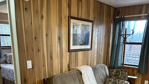 Une pièce chaleureuse avec des boiseries, un canapé agrémenté de coussins à motifs, un tableau encadré au mur et une fenêtre avec des rideaux.