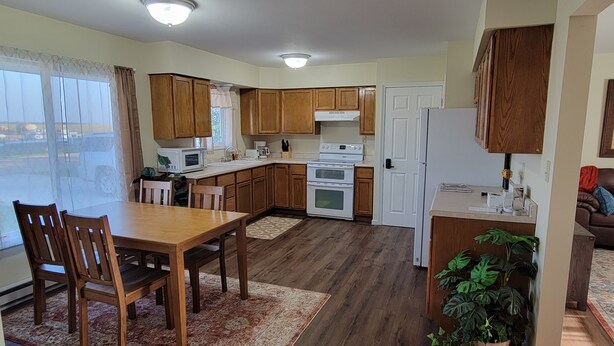 A modern kitchen with wooden cabinets, a dining area with a table and chairs, and a refrigerator.