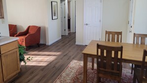 A dining area with a wooden table and chairs, a red armchair, and a kitchen area with wooden cabinets and a countertop.