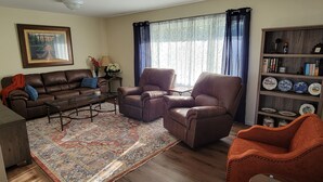 A living room with a brown leather sofa, two brown leather armchairs, a coffee table, a patterned rug, a bookshelf with decorative plates, and a painting on the wall.