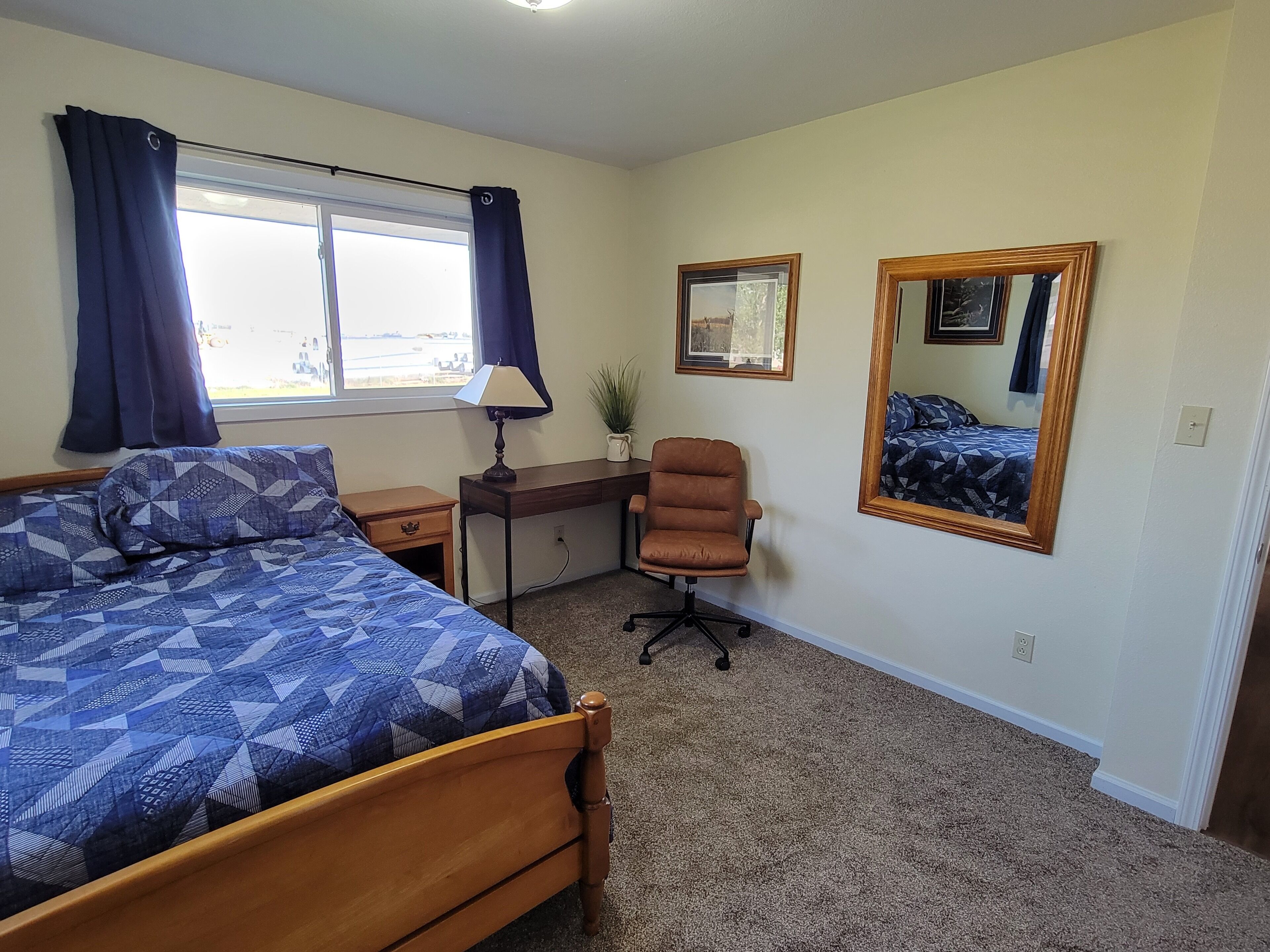 A bedroom with a bed, desk, chair, and a large mirror.