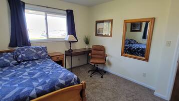 A bedroom with a bed, desk, chair, and a large mirror.