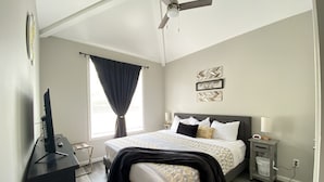 Un dormitorio con cama, escritorio, ventilador de techo, ventana con cortinas y una pared con un cartel.