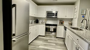 Una cocina con armarios blancos, electrodomésticos de acero inoxidable y piso gris.