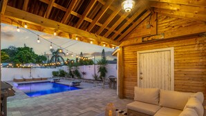 Une terrasse en bois avec une piscine, des sièges d’extérieur et des guirlandes lumineuses.