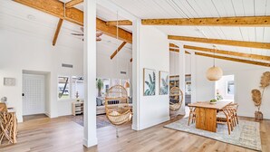 Une pièce spacieuse avec des poutres apparentes, une table à manger en bois avec des chaises, et une grande fenêtre laissant entrer la lumière naturelle.