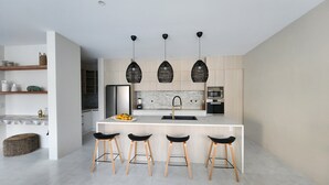 A modern kitchen with a central island, four bar stools, a refrigerator, an oven, and a microwave. - Villa Varia (Rarotonga)