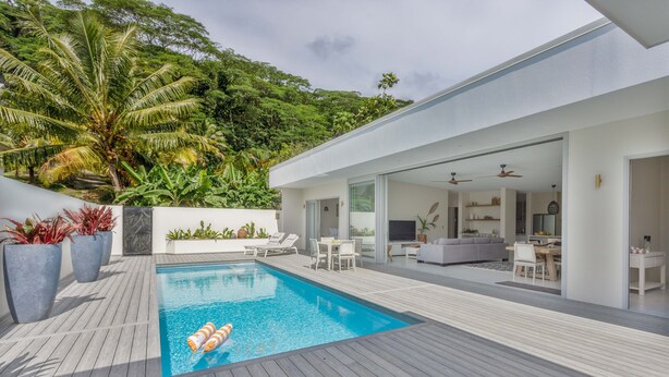 A modern outdoor pool area with a wooden deck, lounge chairs, and a dining area. - Villa Varia (Rarotonga)