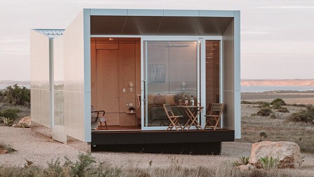 Una casa moderna i minimalista amb una porta de vidre que dona a l'interior, on hi ha un sofà i algunes cadires.